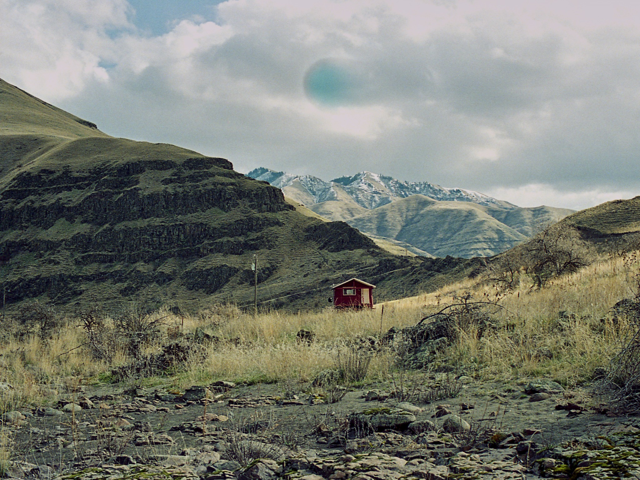A small red cabin beneath rounded mountains